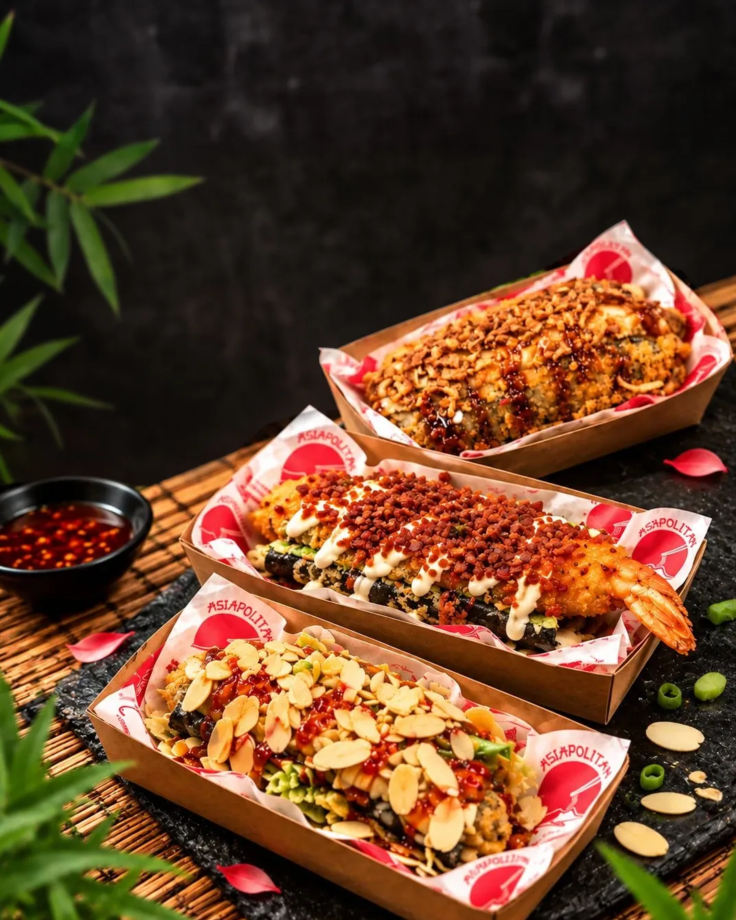 Tre Sushi Dog nelle vaschette Asiapolitan, su una lastra d’ardesia: pollo fritto con mandorle, ebi con gambero fritto e pork con cipolla croccante.